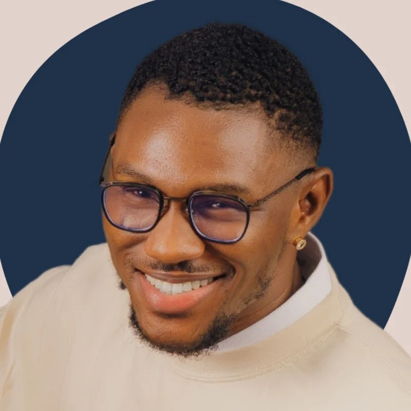 Smiling man with glasses and an earring, wearing a light sweater. Blue background and warm lighting create a cheerful mood.
