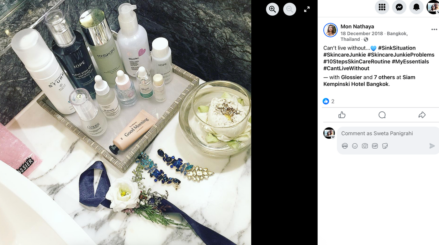 Skincare products on a marble sink, including bottles and jars. Blue and white accents, flowers, and a folded ribbon are nearby.
